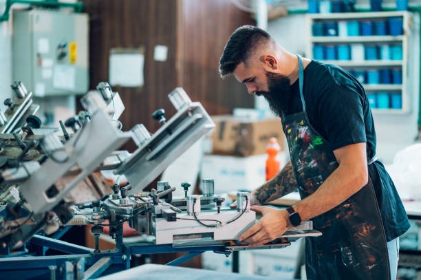Male worker using screen printing film and a printing machine in a workshop